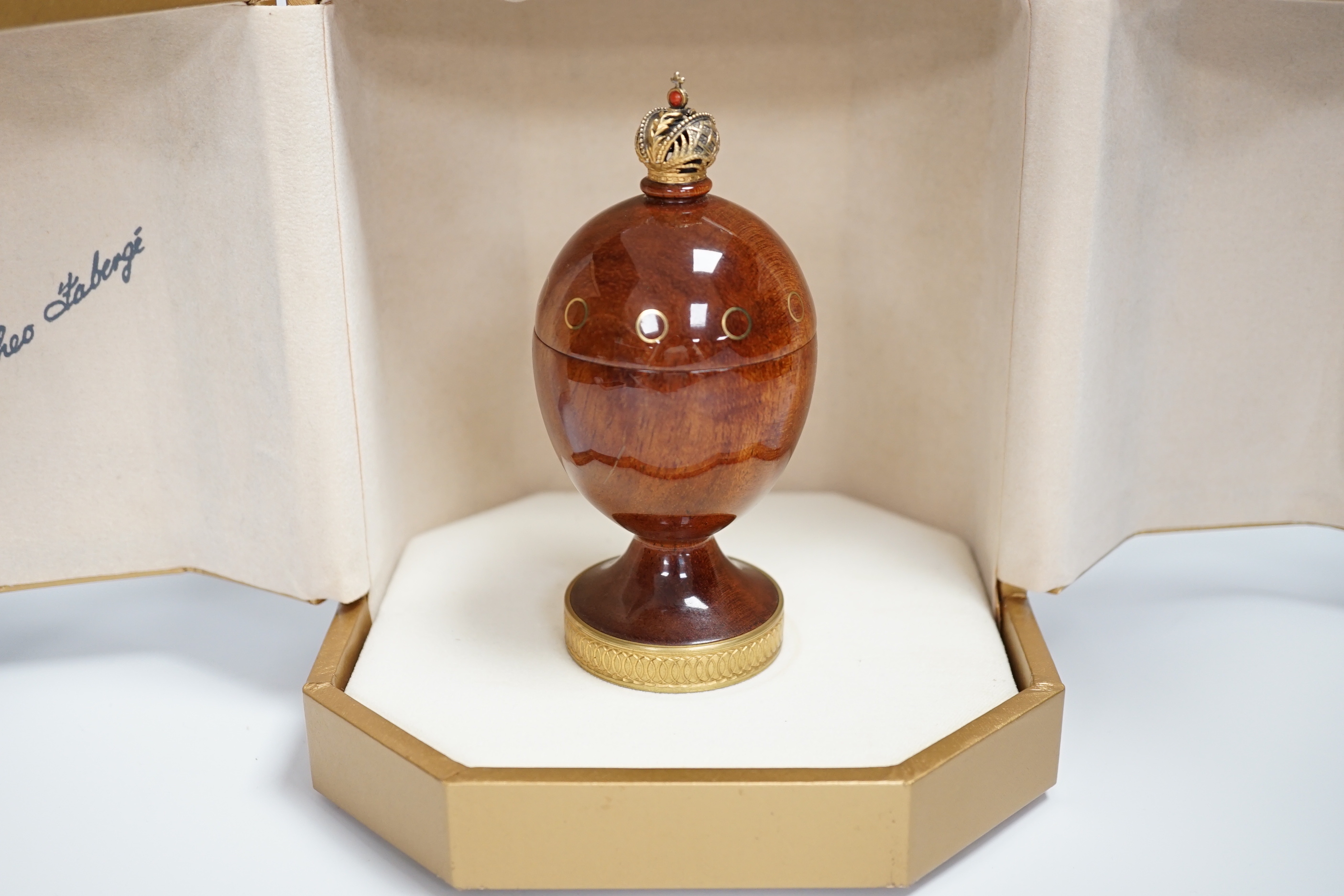 A cased Theo Faberge, (1922-2007) turned bubinga wood Eternity Egg, with Imperial Crown finial, gilt ring decoration and interior blackwood ring tray, with box and paperwork, 13.1cm